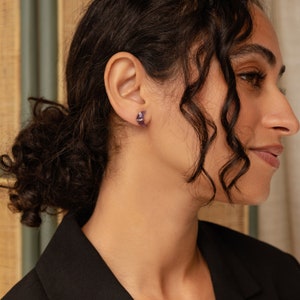 May include: A person wearing a pair of small, purple, crescent moon shaped earrings.