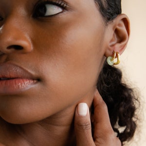 Peut inclure: Gros plan sur l'oreille d'une personne avec deux cr&eacute;oles en or. La cr&eacute;ole du haut a un charme en pierre vert clair.