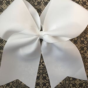 May include: A large white bow made of grosgrain ribbon. The bow is tied with a single loop in the center.