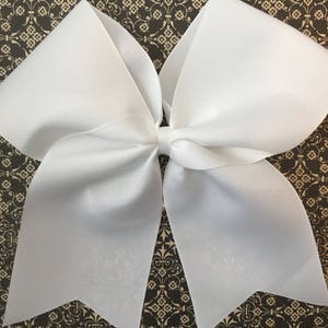 May include: A large white cheer bow with a pointed shape at the bottom. The bow is made of a shiny, smooth fabric.