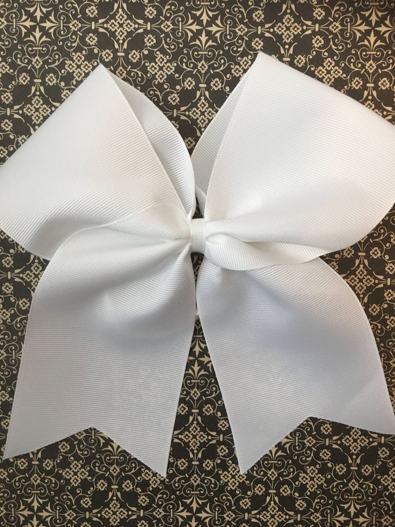May include: A large white cheer bow with a pointed shape at the bottom. The bow is made of a shiny, smooth fabric.