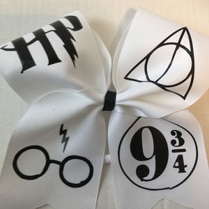 May include: White hair bow with black Harry Potter themed designs. The designs include the Hogwarts crest, glasses, lightning bolt, and the number 9 3/4.