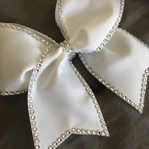 Pu&ograve; includere: Un fiocco da cheerleader bianco con un bordo di strass argentati. Il fiocco &egrave; fatto di un nastro bianco spesso e ha una forma grande e piena.