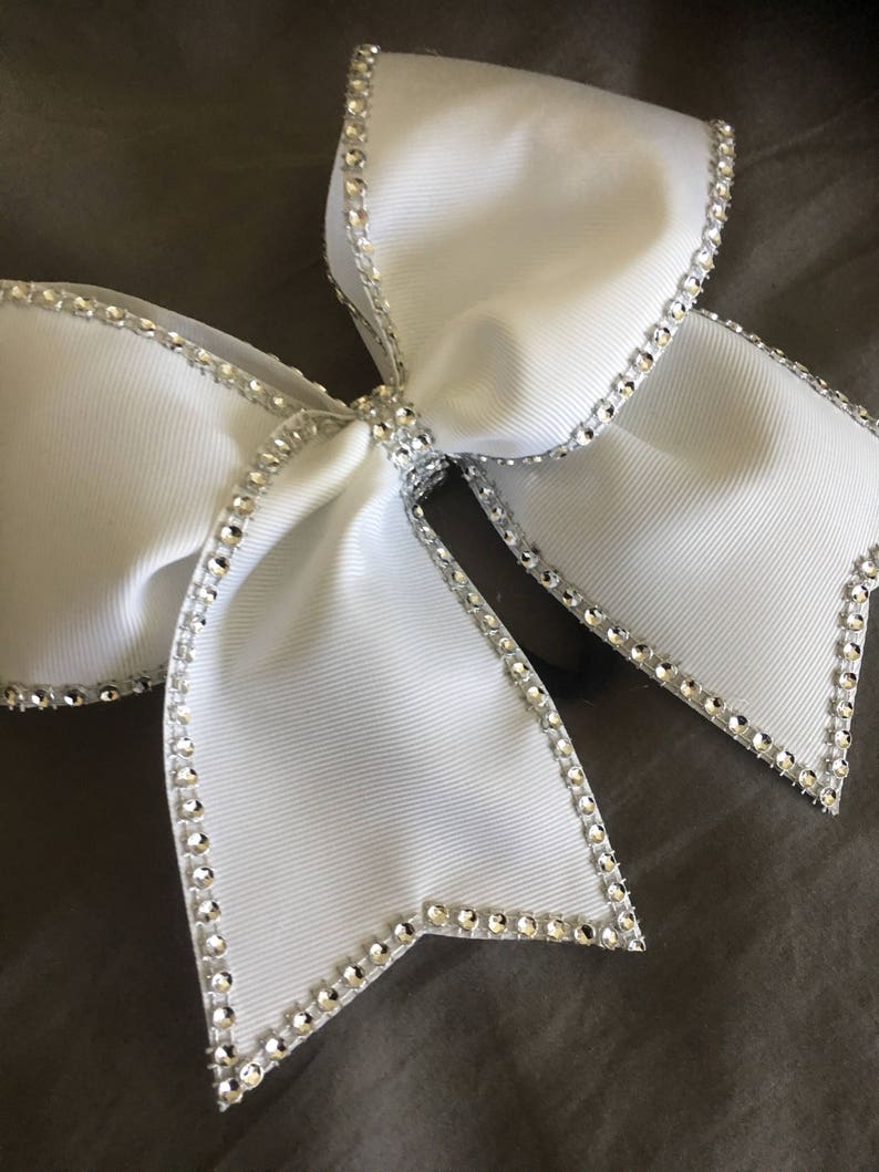 Pu&ograve; includere: Un fiocco da cheerleader bianco con un bordo di strass argentati. Il fiocco &egrave; fatto di un nastro bianco spesso e ha una forma grande e piena.
