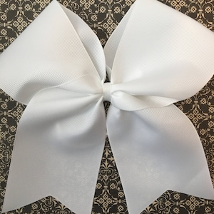 May include: A large white cheer bow with a pointed shape at the bottom. The bow is made of a shiny, smooth fabric.