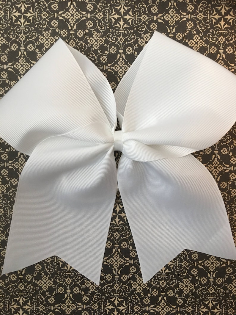 May include: A large white cheer bow with a pointed shape at the bottom. The bow is made of a shiny, smooth fabric.