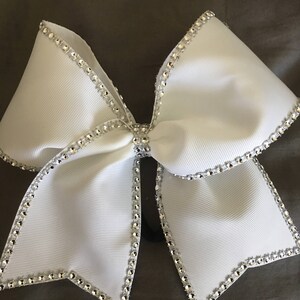 Pu&ograve; includere: Un fiocco da cheerleader bianco con un bordo di strass argentati. Il fiocco &egrave; realizzato in nastro di grosgrain e ha un bordo con filo metallico.