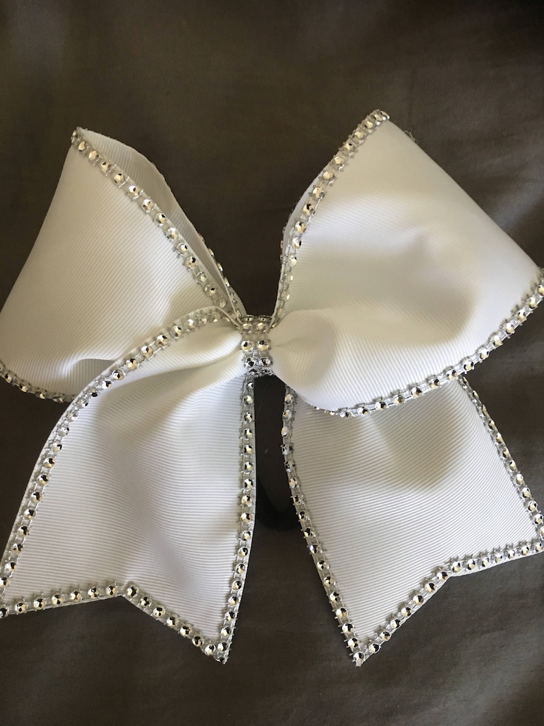 Pu&ograve; includere: Un fiocco da cheerleader bianco con un bordo di strass argentati. Il fiocco &egrave; realizzato in nastro di grosgrain e ha un bordo con filo metallico.