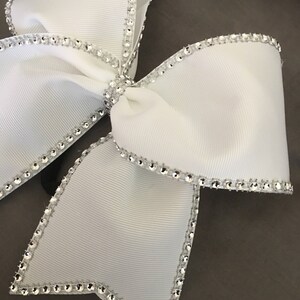 Pu&ograve; includere: Un fiocco bianco con un bordo di strass argentati. Il fiocco &egrave; realizzato in un tessuto morbido e setoso ed &egrave; perfetto per aggiungere un tocco di brillantezza a qualsiasi outfit.
