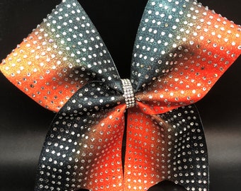 May include: A large black, orange, and silver cheer bow with a gradient of color. The bow is covered in rhinestones.