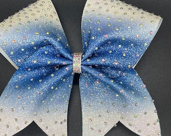 May include: A large blue and white ombre cheer bow with iridescent rhinestones. The bow is made of glitter fabric and has a white center.