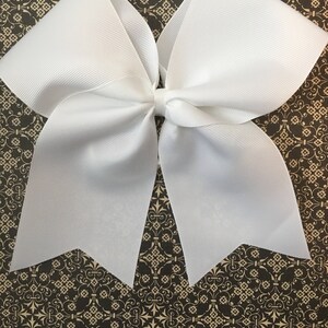 May include: A large white cheer bow with a pointed shape at the bottom. The bow is made of a shiny, textured fabric.