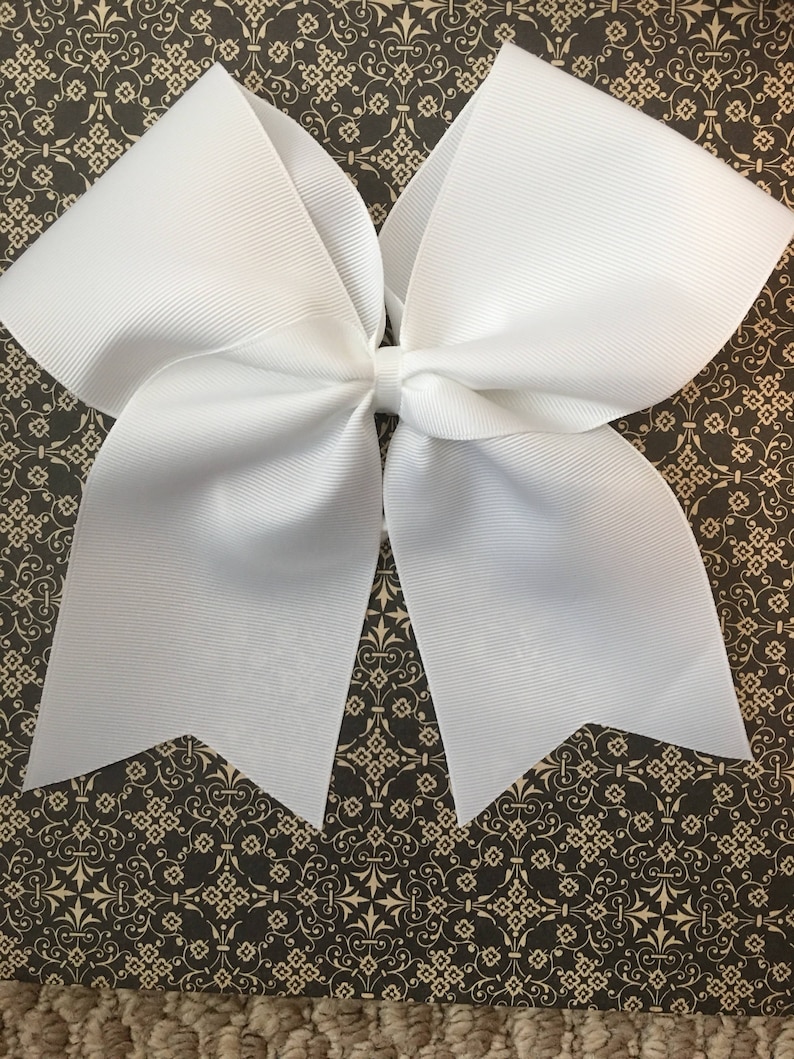 May include: A large white cheer bow with a pointed shape at the bottom. The bow is made of a shiny, textured fabric.