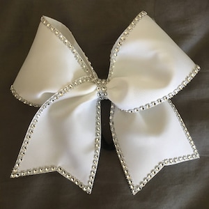 Pu&ograve; includere: Un fiocco da cheerleader bianco con un bordo di strass argentati. Il fiocco &egrave; legato in una forma classica con due anelli e un nodo centrale.