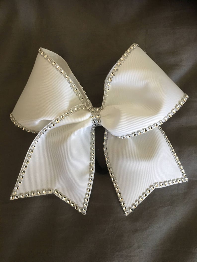Pu&ograve; includere: Un fiocco da cheerleader bianco con un bordo di strass argentati. Il fiocco &egrave; legato in una forma classica con due anelli e un nodo centrale.