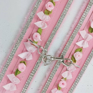 Op de afbeelding: Roze en witte hondenriem met zilveren strass steentjes en roze bloemenversieringen.