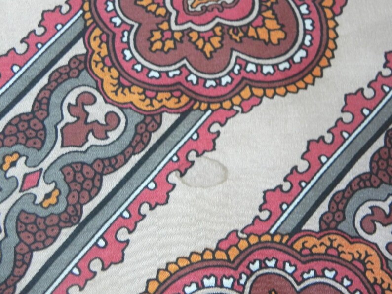 May include: Close-up of a patterned fabric with a beige background. The design features repeating floral and geometric shapes in red, brown, orange, and grey. Diagonal stripes with white borders intersect the pattern.