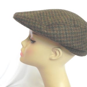 May include: Brown tweed flat cap with a classic design. The cap features a traditional herringbone pattern in shades of brown and black. This hat is a stylish accessory for various occasions.