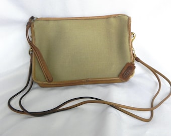 May include: A rectangular crossbody bag with a tan canvas body and brown leather trim. The bag has a long, thin strap and a small leather tag. The hardware is gold-toned.