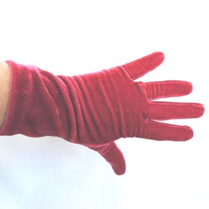May include: A single red velvet glove, with a long sleeve, is shown against a white background. The glove is a vibrant shade of red, with a soft, textured appearance. The fingers are fully extended, showcasing the glove's shape and design.