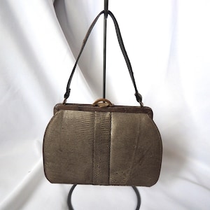 Könnte beinhalten: Eine Vintage-Handtasche mit einem strukturierten, reptilienartigen Muster in Olivgrün und Braun. Die Tasche hat einen dunkelbraunen Rahmen, einen goldfarbenen Verschluss und einen schwarzen Griff. Die Tasche wird vor einem weißen Hintergrund präsentiert.