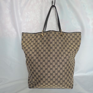 Puede incluir: Un bolso tote de lona en color beige y marrón oscuro con un patrón repetitivo de monogramas GG entrelazados. El bolso cuenta con dos correas de hombro de cuero marrón oscuro sujetas con herrajes metálicos dorados, una abertura superior.