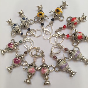 May include: A set of 10 silver teapot earrings with colorful floral and geometric designs. Each earring features a teapot charm with a different pattern and is attached to a silver hook.