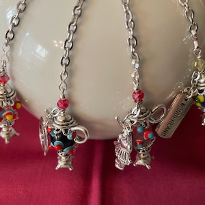 May include: Four decorative tea infusers with silver chains and charms. Each charm is a miniature teapot or teacup, adorned with colorful beads and intricate details. One charm has the word "Wonderland" on it.