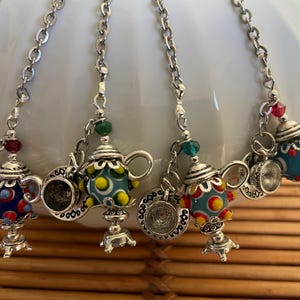 May include: Five silver charm necklaces with teapot pendants. Each teapot is decorated with colorful, geometric patterns in blue, red, yellow, and green.