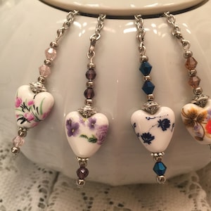 May include: Four porcelain heart tea bag charms with floral designs. Each charm has a silver chain and a crystal bead.