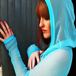May include: A woman wearing a light blue mesh hooded top with a blue trim. The top has long sleeves and a loose fit.