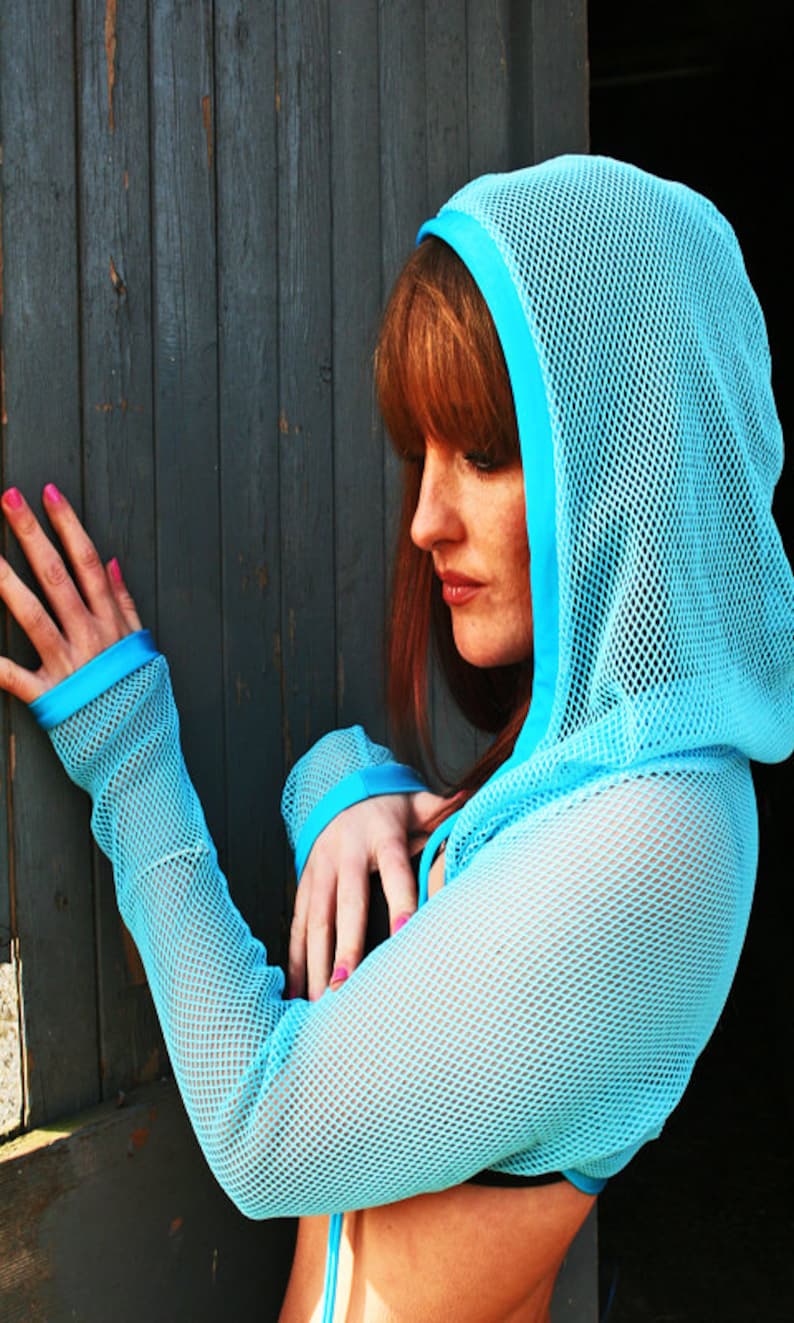 May include: A woman wearing a light blue mesh hooded top with a blue trim. The top has long sleeves and a loose fit.