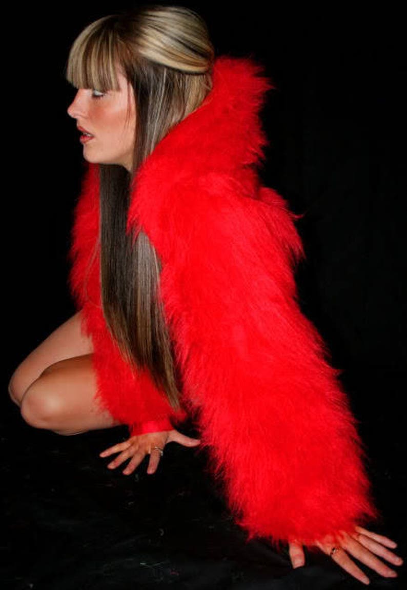 May include: A woman wearing a red fluffy jacket with a hood. She has long brown hair with blonde highlights and is posing with her hands on the floor.