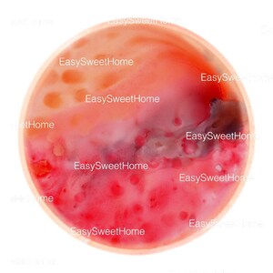 Puede incluir: Un primer plano de un cuenco redondo de madera lleno de un líquido rojo vibrante. El líquido tiene un patrón abstracto en espiral con toques de naranja y rosa. El cuenco está ligeramente inclinado, lo que permite vislumbrar el fondo blanco.