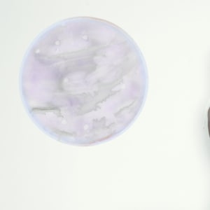 Puede incluir: Una mujer con un vestido blanco se sienta en un armario blanco con un fondo blanco. Dos círculos abstractos de acuarela están en la pared detrás de ella.