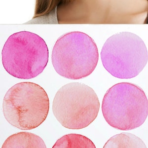 Op de afbeelding: Een wit rechthoekig kunstwerk met twaalf roze aquarel cirkels in verschillende tinten. De tekst "Size 2" staat in de linkerbovenhoek. Het kunstwerk wordt door een persoon vastgehouden.