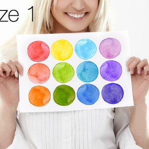 Puede incluir: Una tarjeta blanca con 12 círculos de acuarela en un patrón de arcoíris. Los círculos están dispuestos en cuatro filas de tres. La tarjeta está sostenida por las manos de una persona.