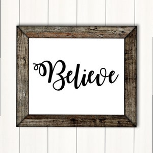Könnte beinhalten: Ein gerahmtes Schild mit dem Wort "Believe" in einer dekorativen Schreibschrift auf weißem Hintergrund. Der Rahmen ist aus rustikalem Holz mit einer dunkelbraunen Beize.