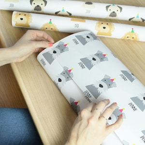 May include: White wrapping paper with a repeating pattern of gray schnauzer dogs wearing pink party hats. The paper has the name "Penny" printed on it.