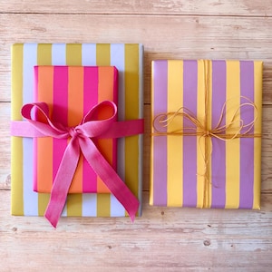 May include: Two wrapped gifts with colorful striped paper. One gift is wrapped in yellow and white stripes, with a smaller gift in pink and orange stripes, tied with a pink ribbon. The other gift is yellow and purple striped, tied with twine.