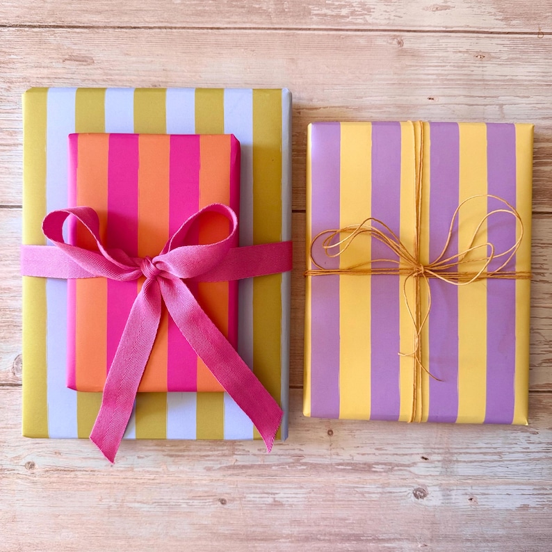 May include: Two wrapped gifts with colorful striped paper. One gift is wrapped in yellow and white stripes, with a smaller gift in pink and orange stripes, tied with a pink ribbon. The other gift is yellow and purple striped, tied with twine.