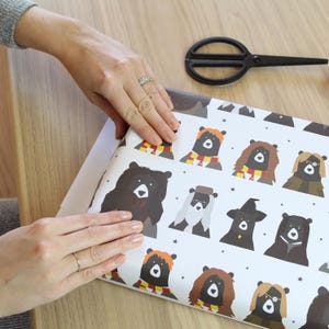 May include: White wrapping paper with a repeating pattern of black bears dressed as characters from the Harry Potter series. The bears are wearing hats, scarves, and glasses.