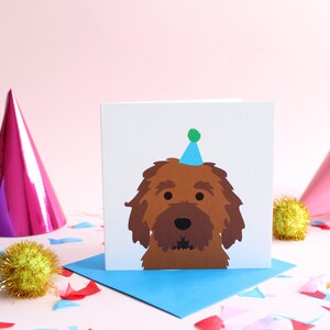 Peut inclure: Carte de vœux carrée avec un chien marron portant un chapeau de fête bleu. La carte est posée sur une enveloppe bleue, avec des chapeaux de fête et des confettis. Idéale pour un anniversaire.