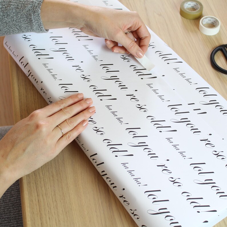 May include: White wrapping paper with the text "lol you're so old!" repeated in black cursive writing.