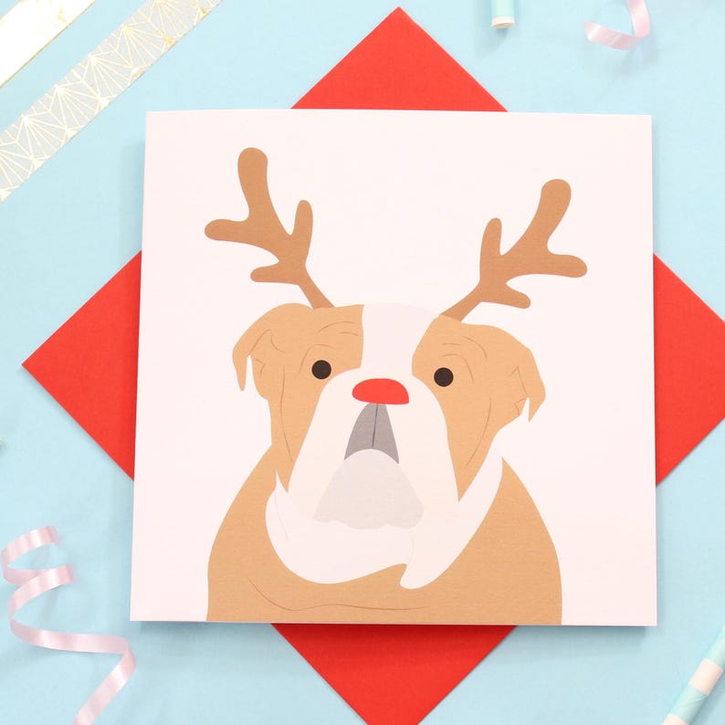May include: A white card with a brown and white bulldog wearing a red reindeer antler headband. The card is on a red and blue background.