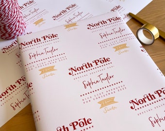 May include: White wrapping paper with a red and gold design. The paper features the text "North Pole Special Delivery For: Sophia Taylor Nice List Approved For Christmas 2022 From Santa".