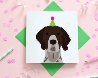 May include: A white card with a brown and white dog wearing a green and pink party hat. The card has a green background.