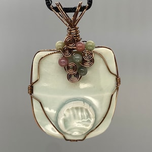 May include: A white ceramic pendant with a handprint design, wrapped in copper wire and accented with green, pink, and brown beads.