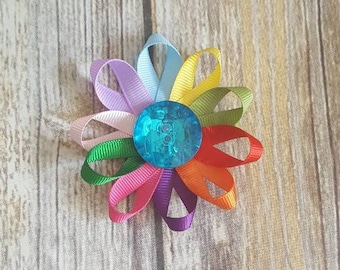May include: A rainbow-colored flower made of ribbon with a blue button in the center.
