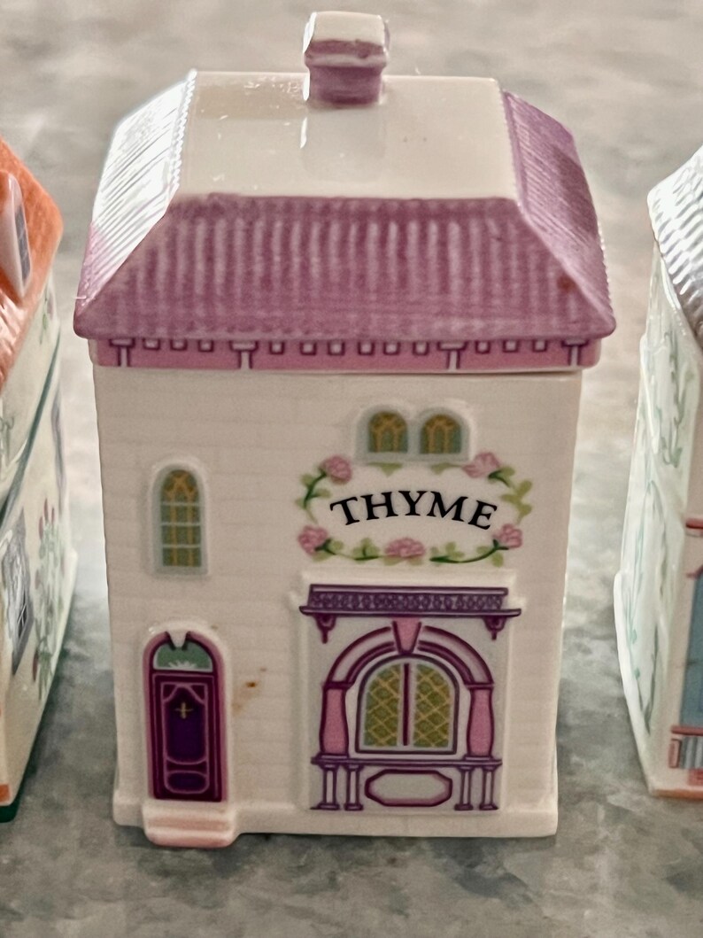 May include: A white ceramic spice jar shaped like a house with a pink roof and a sign that reads "THYME".